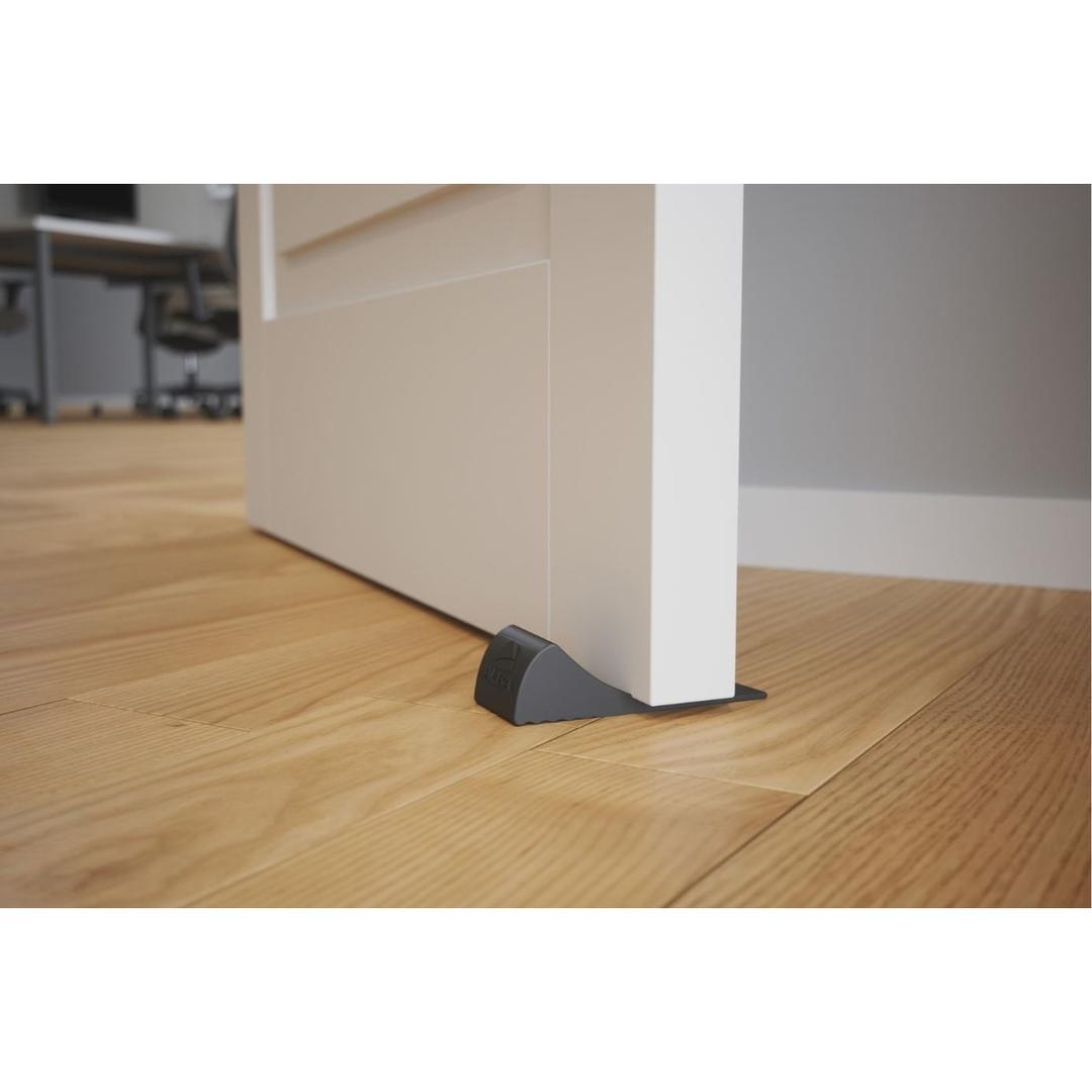 En élastomère antidérapant, noire Cale-porte DOORPOP1 ALBA - Cale-porte ALBA DOORPOP1 glissée sous une porte sur parquet