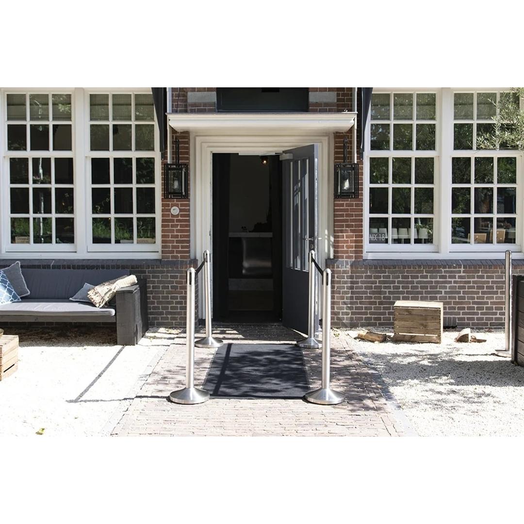 Avec socle, inox brossé, sangle noire Poteau de guidage RETRACTABLE SECURIT - Poteaux Securit RETRACTABLE à sangle noire devant l'entrée d'un restaurant