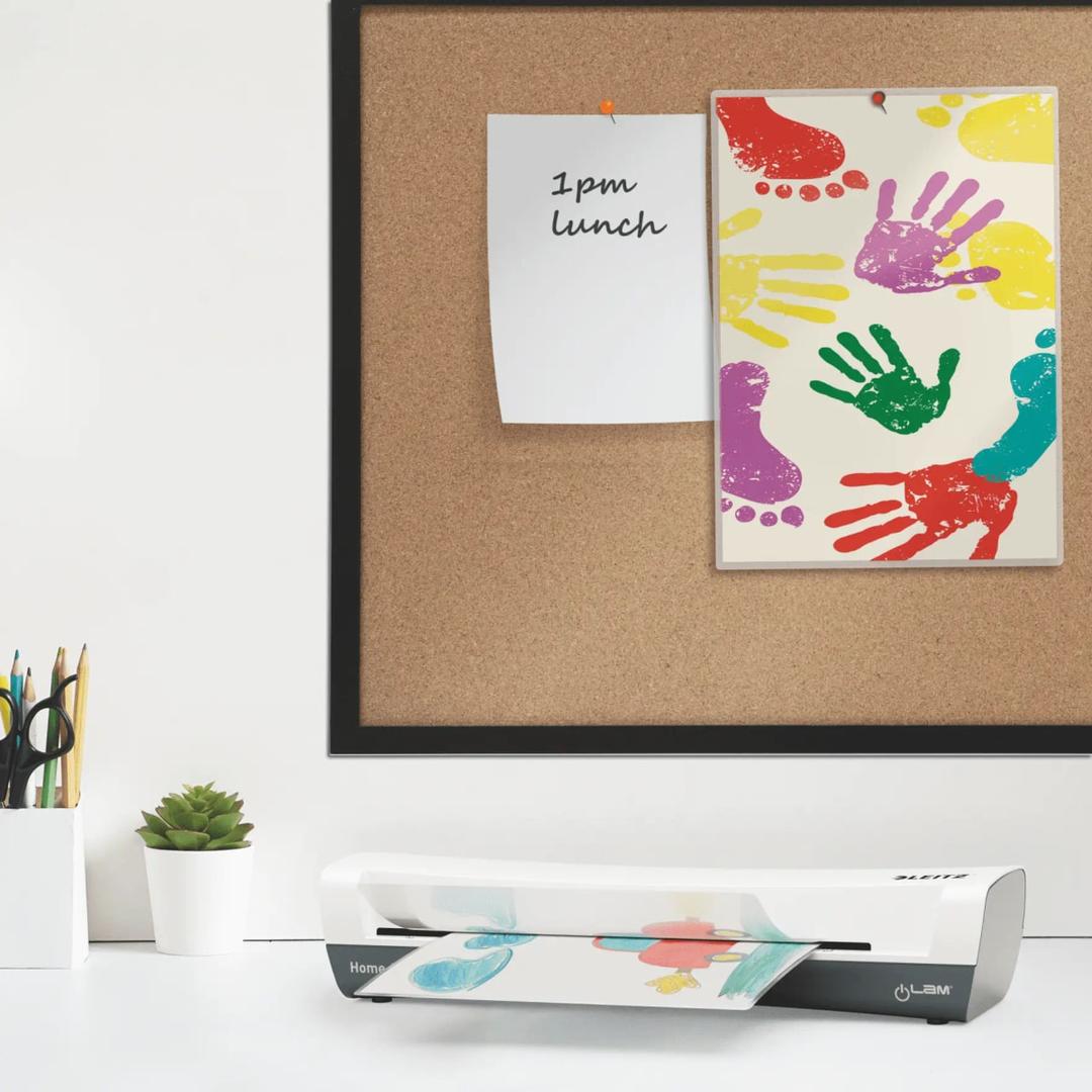 La plastifieuse à pochettes Leitz iLAM Home A3 posée sur un bureau, un document engagé dans la fente