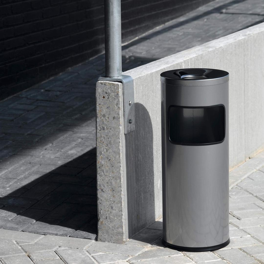 Cendrier-poubelle à couvercle étouffoir, 17 litres SAFE argent métallisé DURABLE - Cendrier-poubelle à couvercle étouffoir DURABLE SAFE argent métallisé, en situation devant un bâtiment