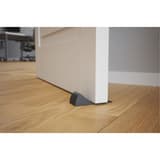 En élastomère antidérapant, noire Cale-porte DOORPOP1 ALBA - Cale-porte ALBA DOORPOP1 glissée sous une porte sur parquet