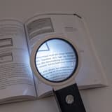 à main ou de table, x 2,5 et x 10 Loupe éclairée LED et UV à pied pliable WEDO - Loupe WEDO à pied pliable posée sur un livre