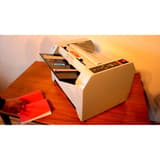Plieuse-agrafeuse de livrets, 15 feuilles SF-2 SUPERFAX - Plieuse-agrafeuse Superfax SF-2 en marche sur un bureau, un livret agrafé posé devant