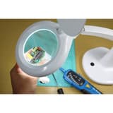 Lampe loupe LED, 2 lentilles MINI ZOOM UNILUX - Lampe loupe LED UNILUX MINI ZOOM blanc, en situation, loupe au-dessus d'un ouvrage