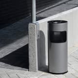 Cendrier-poubelle à couvercle étouffoir, 17 litres SAFE argent métallisé DURABLE - Cendrier-poubelle à couvercle étouffoir DURABLE SAFE argent métallisé, en situation devant un bâtiment