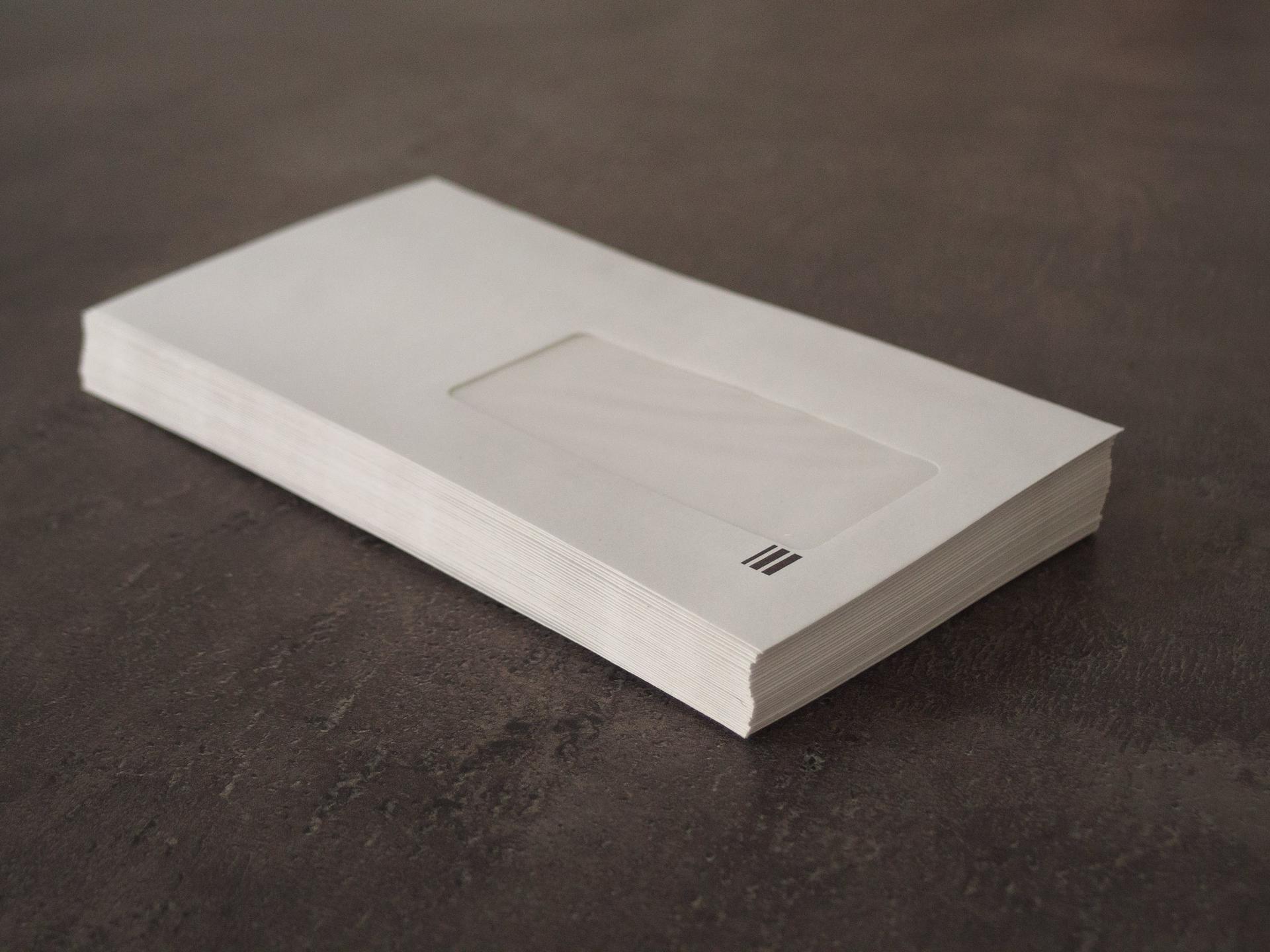 Pile d'enveloppes blanches à fenêtre posée sur un plan de travail gris