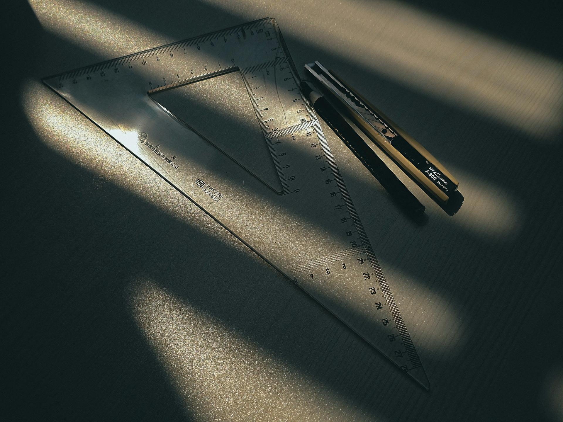 Équerre transparente et cutter posés sur un plan de travail, dans un rayon de soleil